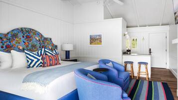 Un dormitorio con una cama grande, un ventilador de techo, un escritorio con taburetes y un cuadro en la pared.