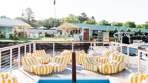 A pool area with yellow and white striped lounge chairs and a flagpole with an American flag.