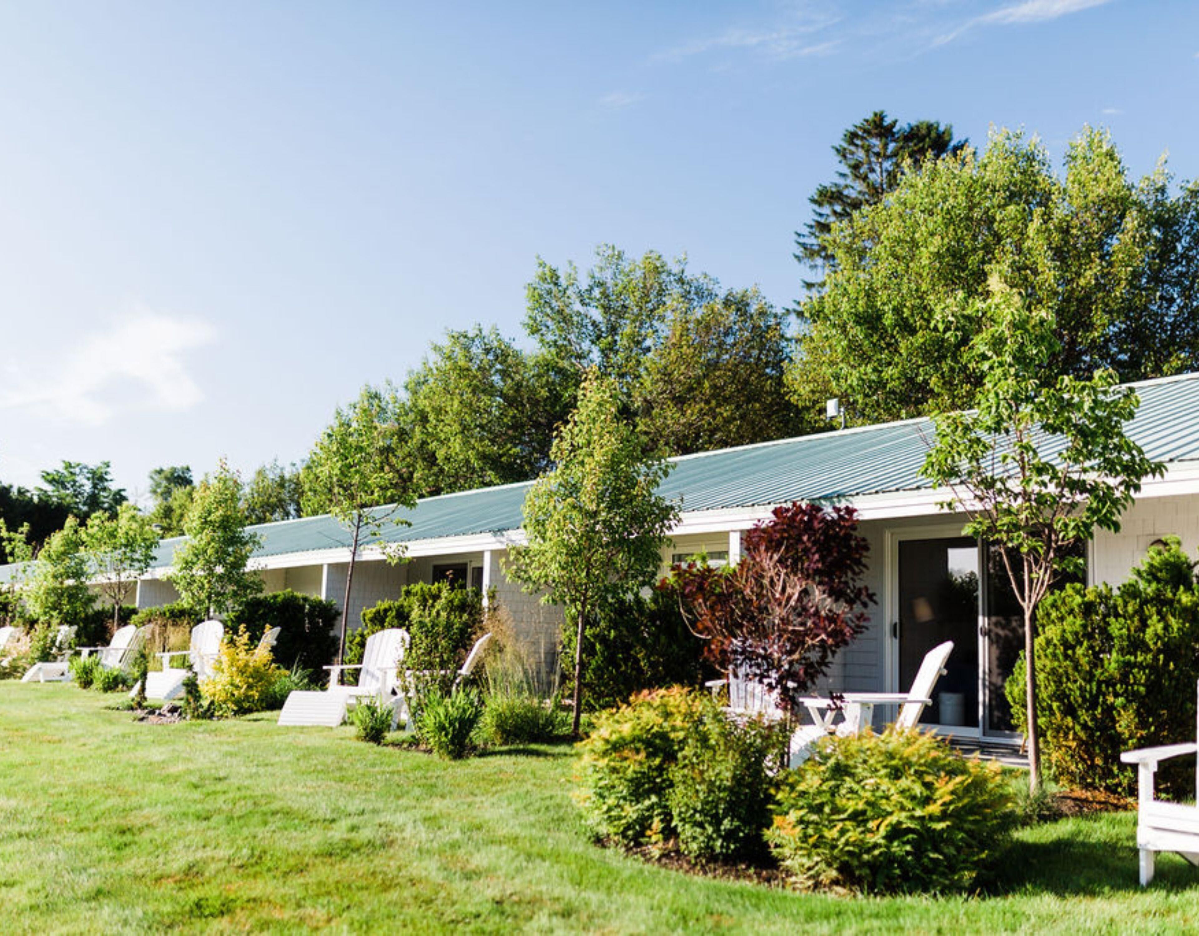 A row of motel buildings with green roofs, white walls, and white outdoor seating.