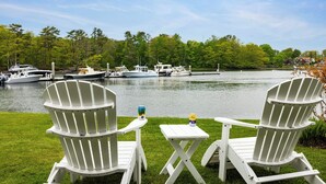 Two white Adirondack chairs facing a lake with boats docked.
