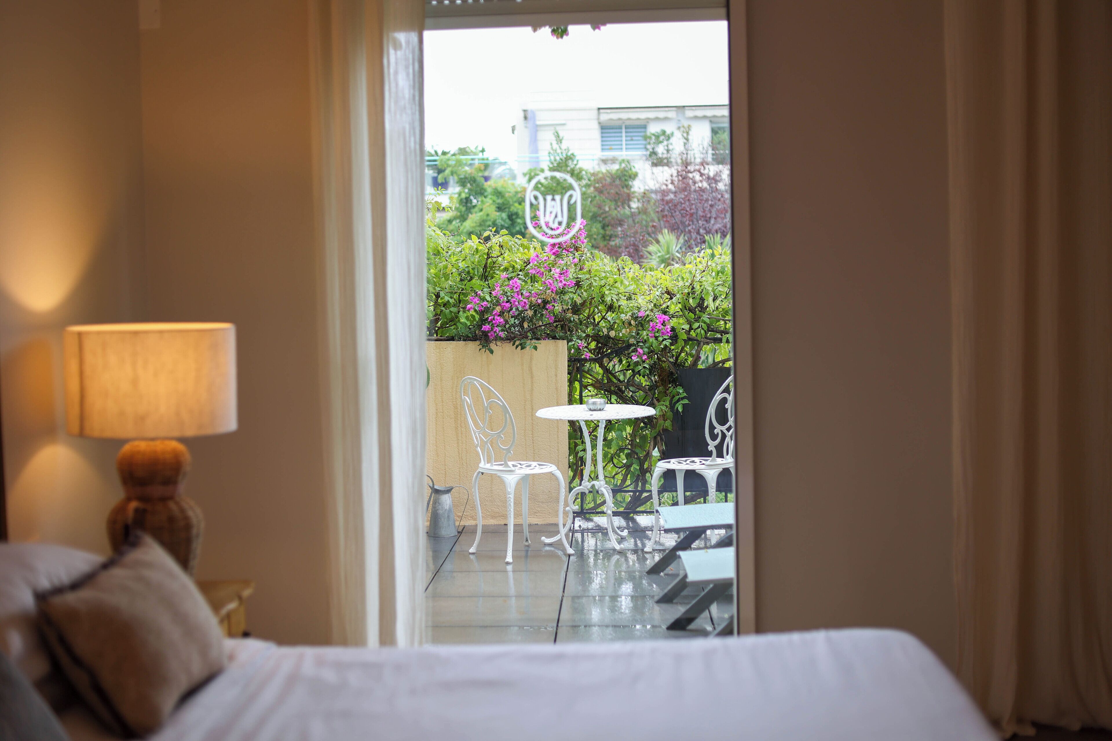 Una camera d'albergo con un letto, una lampada e vista su un patio esterno con sedie e un tavolo.