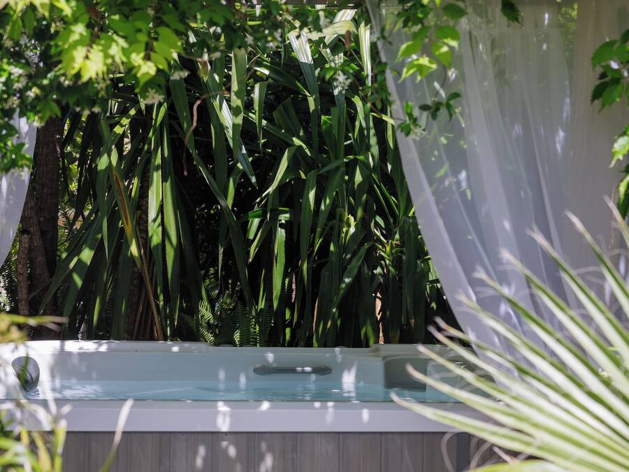 A hot tub surrounded by lush greenery and a wooden fence.