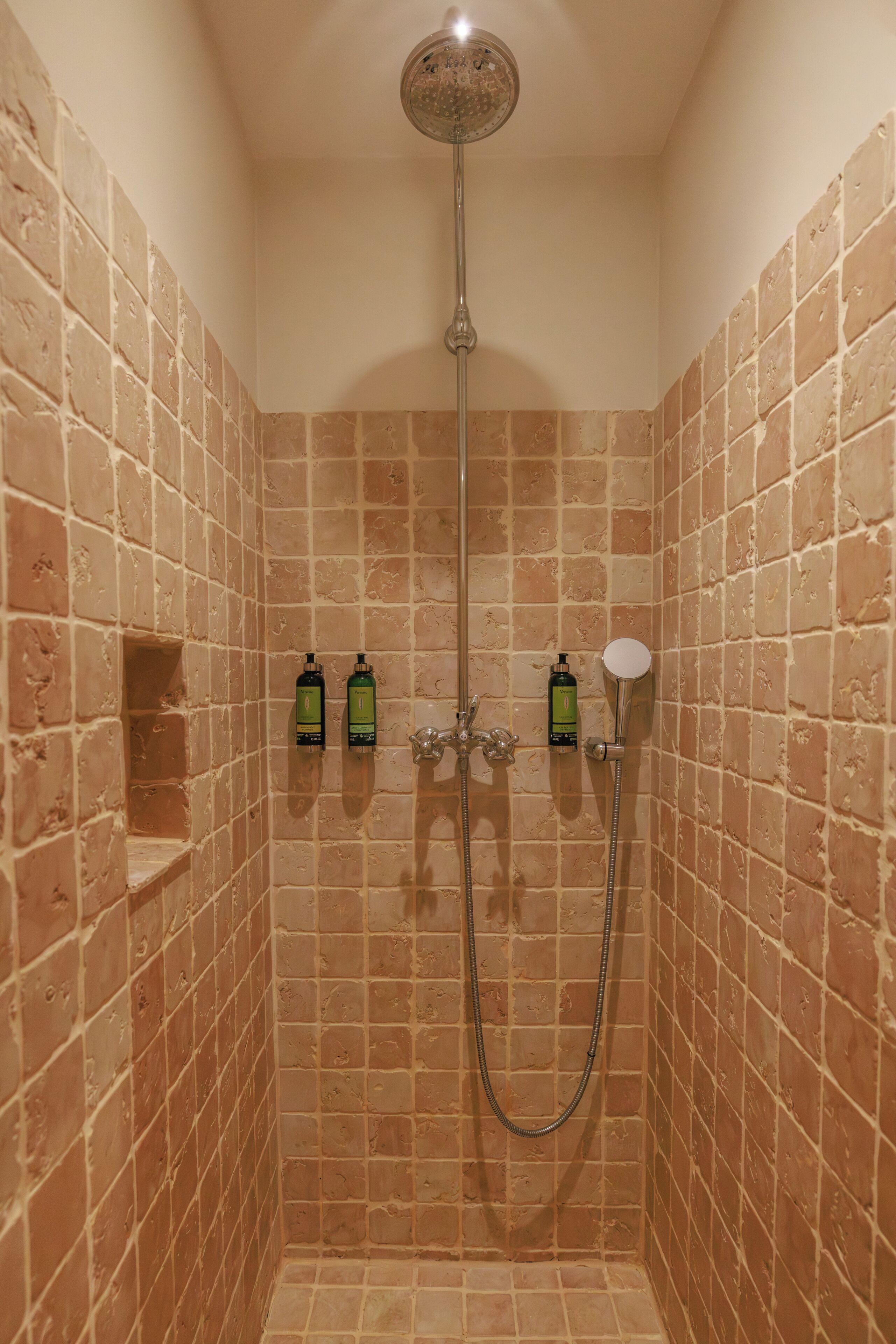 A shower with a handheld showerhead, two bottles of shampoo, and a handheld showerhead.