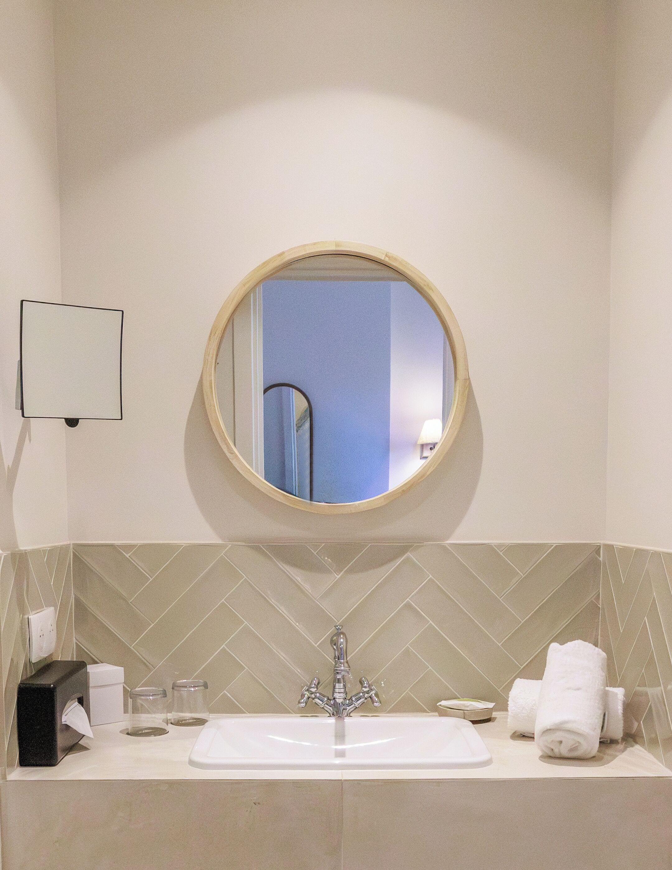 A bathroom with a round mirror, a sink, and a towel rack.
