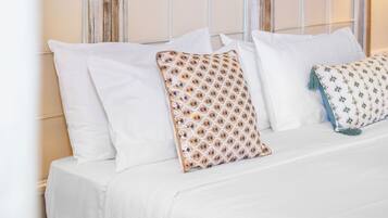 Una cama con ropa de cama blanca y almohadas estampadas, un cabecero color beige y una pared con un diseño de arco decorativo.