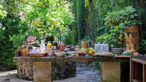 A stone table set with a variety of food items and drinks in a lush garden setting. - Hôtel La Villa Sainte Valérie Adults Only (Antibes)