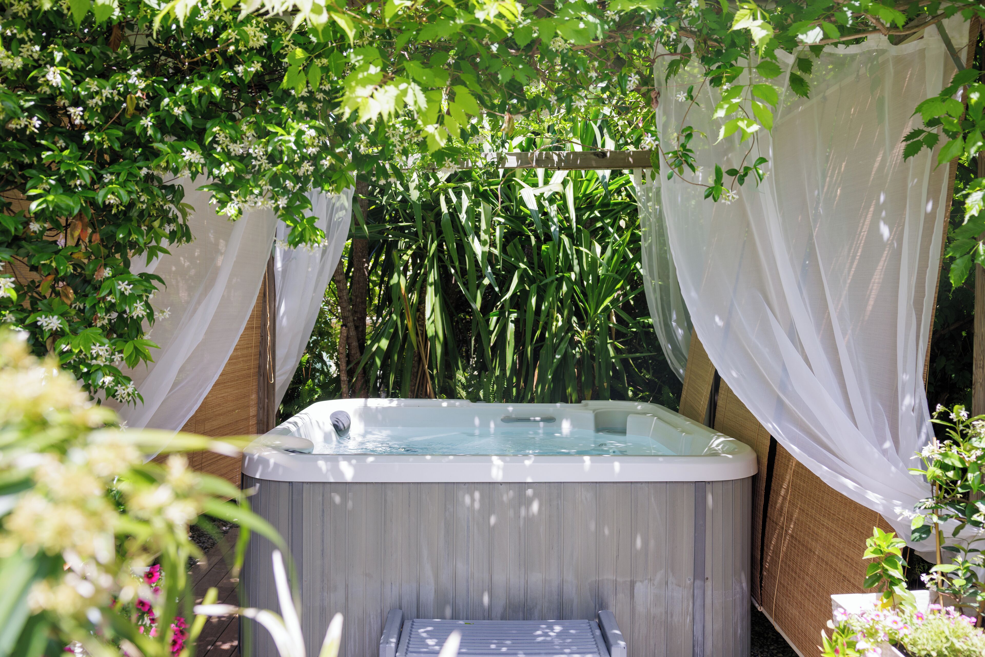 A hot tub surrounded by greenery and white drapes.