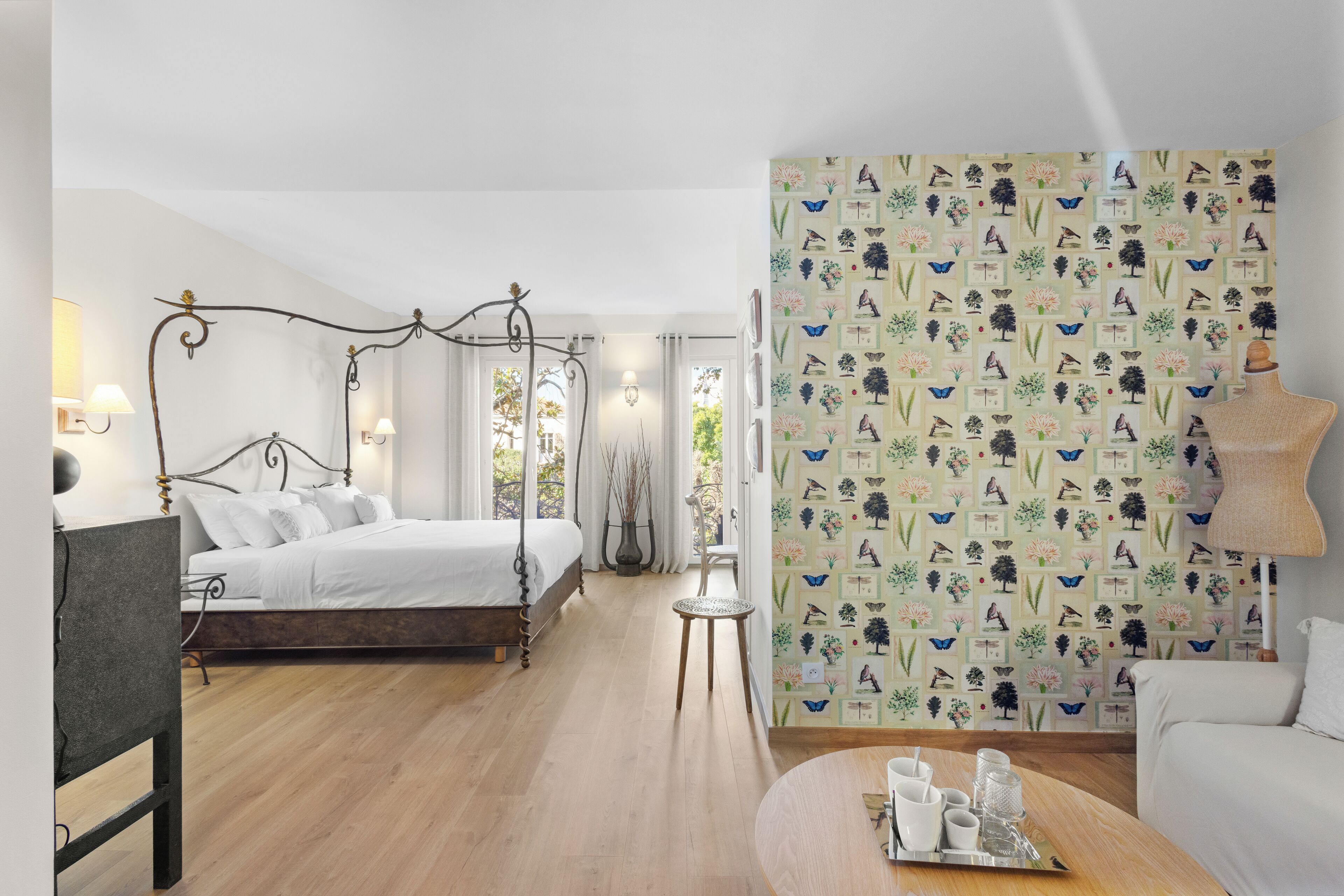 Een slaapkamer met een hemelbed, een klein tafeltje met kopjes en een dienblad, en behang met een patroon.