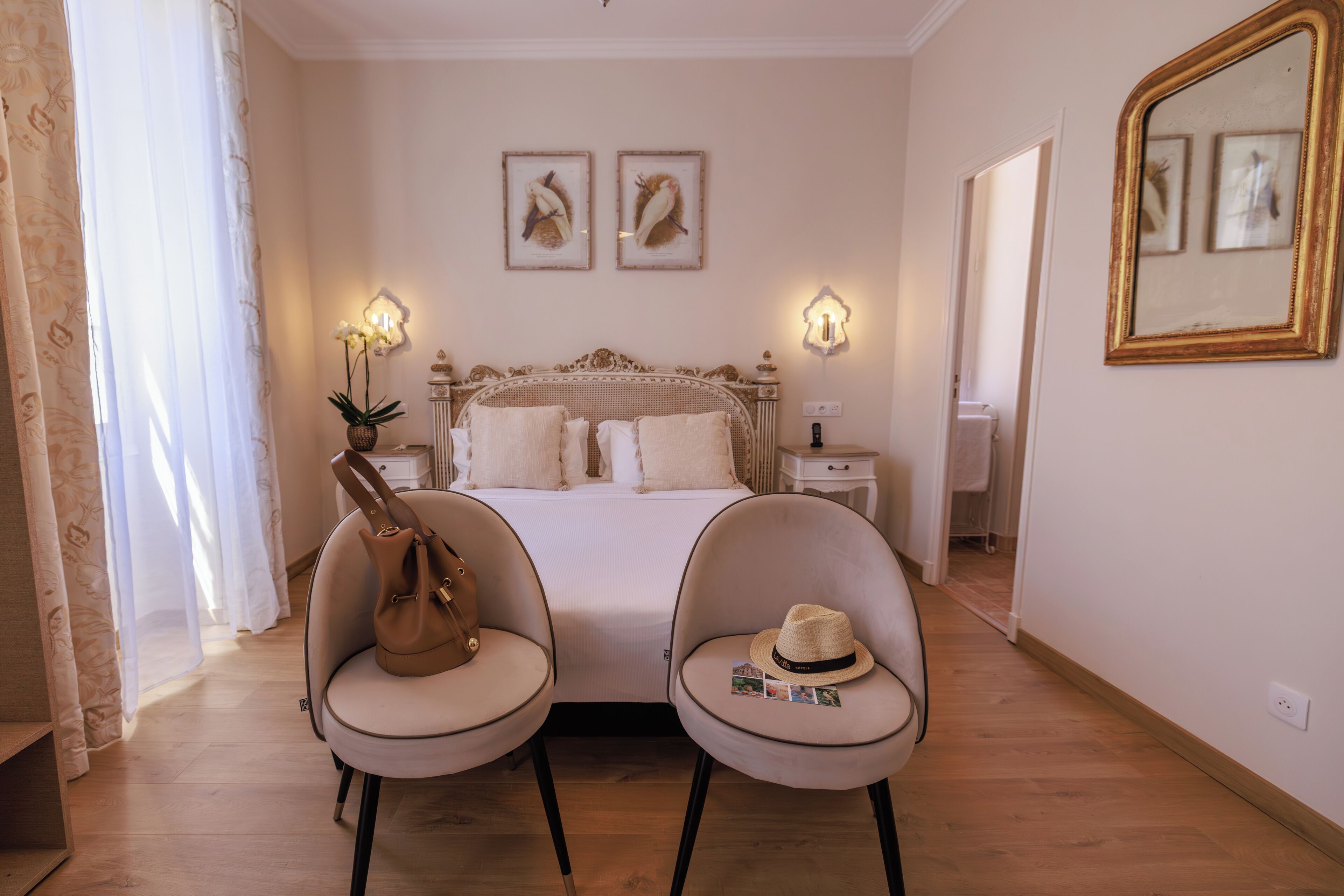 A bedroom with a bed, two chairs, a nightstand, a lamp, and a mirror.