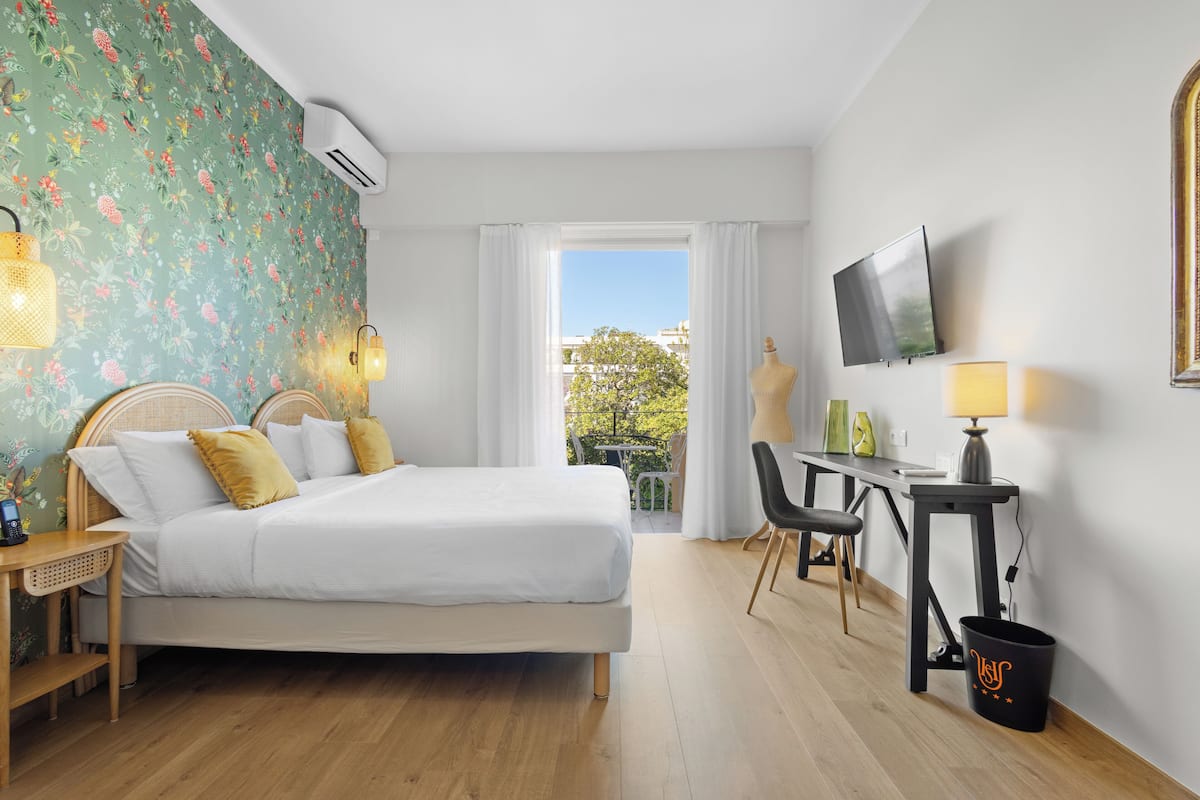 Une chambre d’hôtel équipée d’un lit, d’un bureau, d’une chaise, d’une télévision et d’une fenêtre donnant sur l’extérieur.