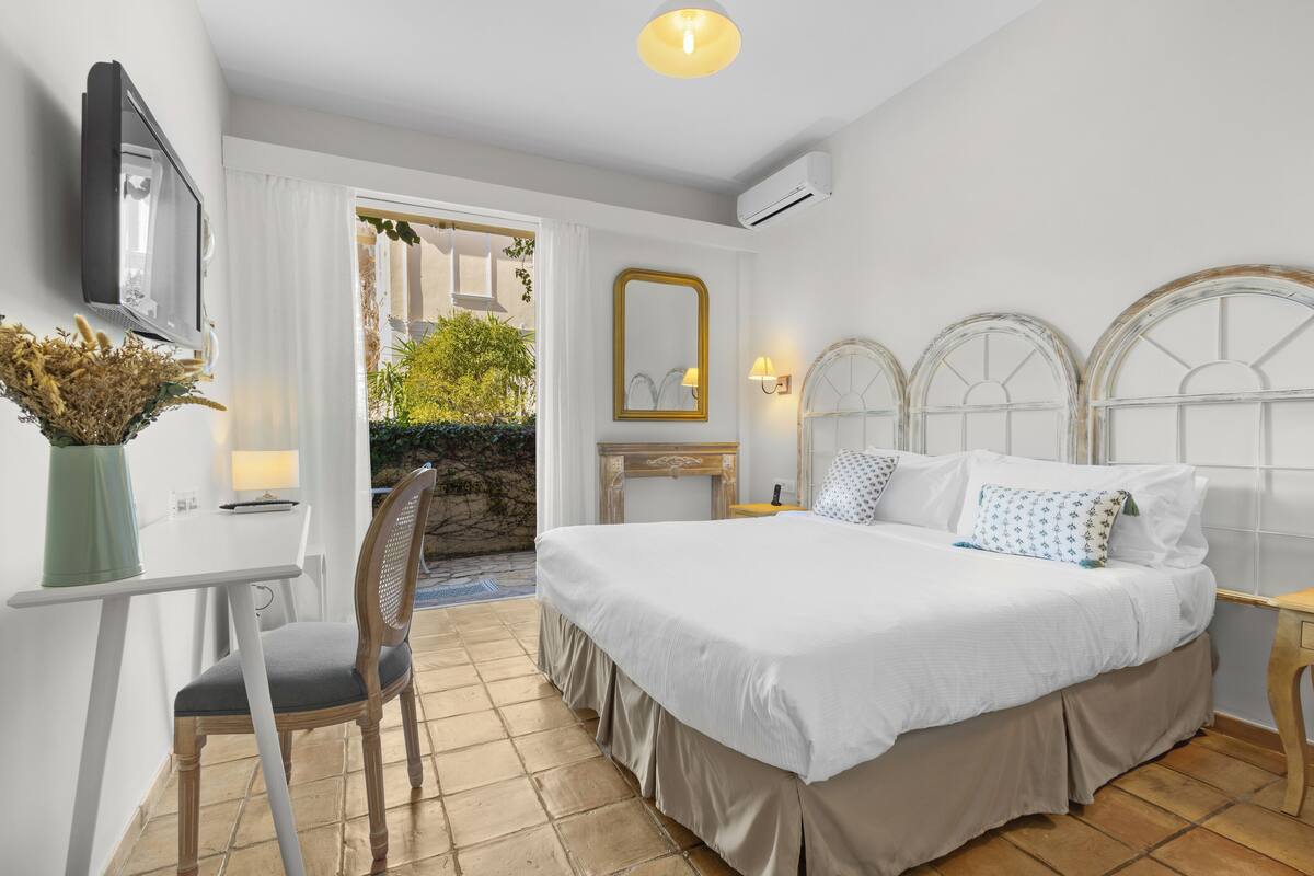 Une chambre à coucher avec un lit, un bureau, une chaise, un miroir et une fenêtre avec des rideaux.