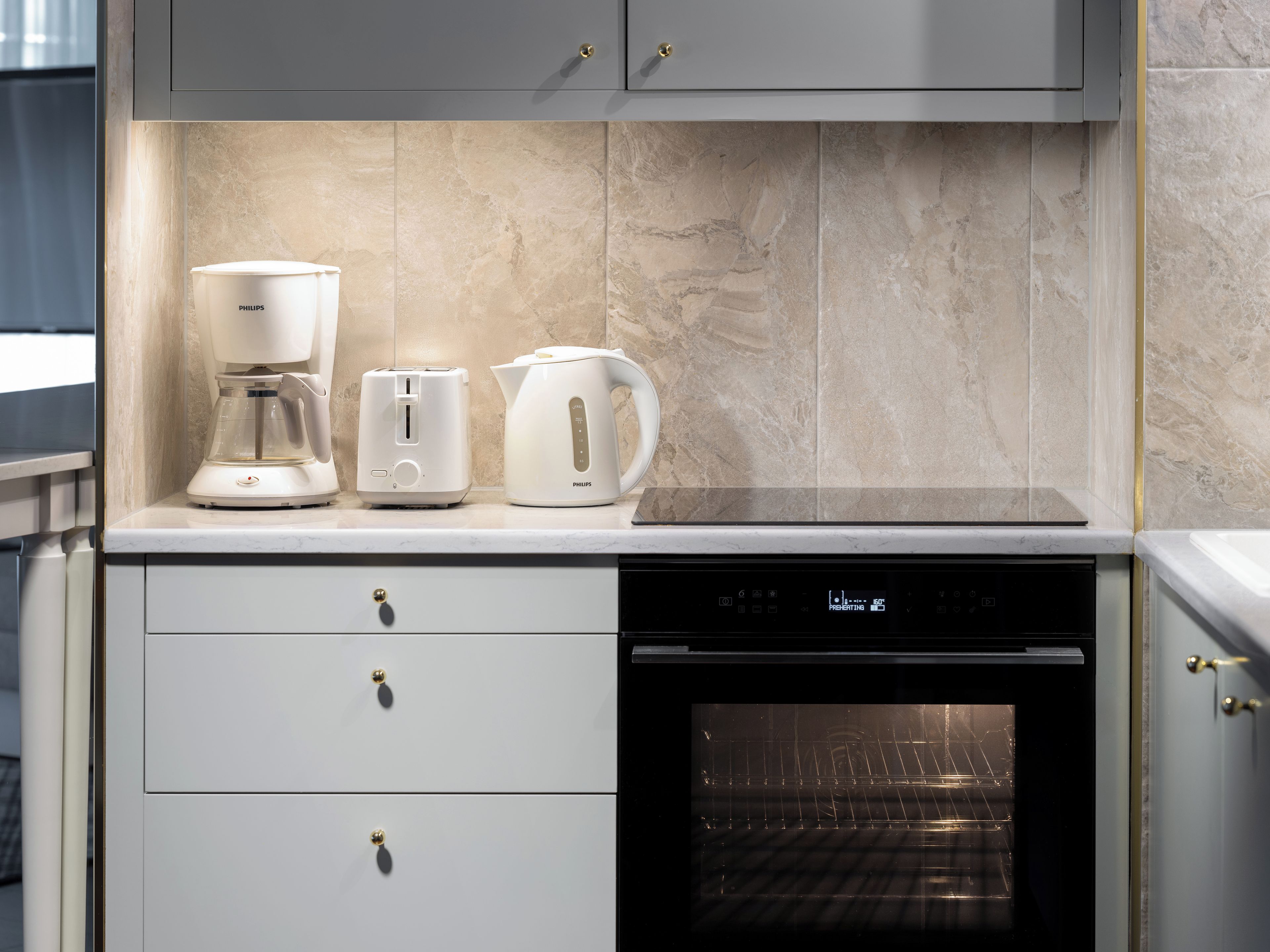 A kitchen with a coffee maker, toaster, and kettle on the countertop, a dishwasher below, and an oven to the right.