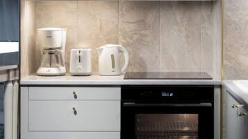 A kitchen with a coffee maker, toaster, and kettle on the countertop, a dishwasher below, and an oven to the right.