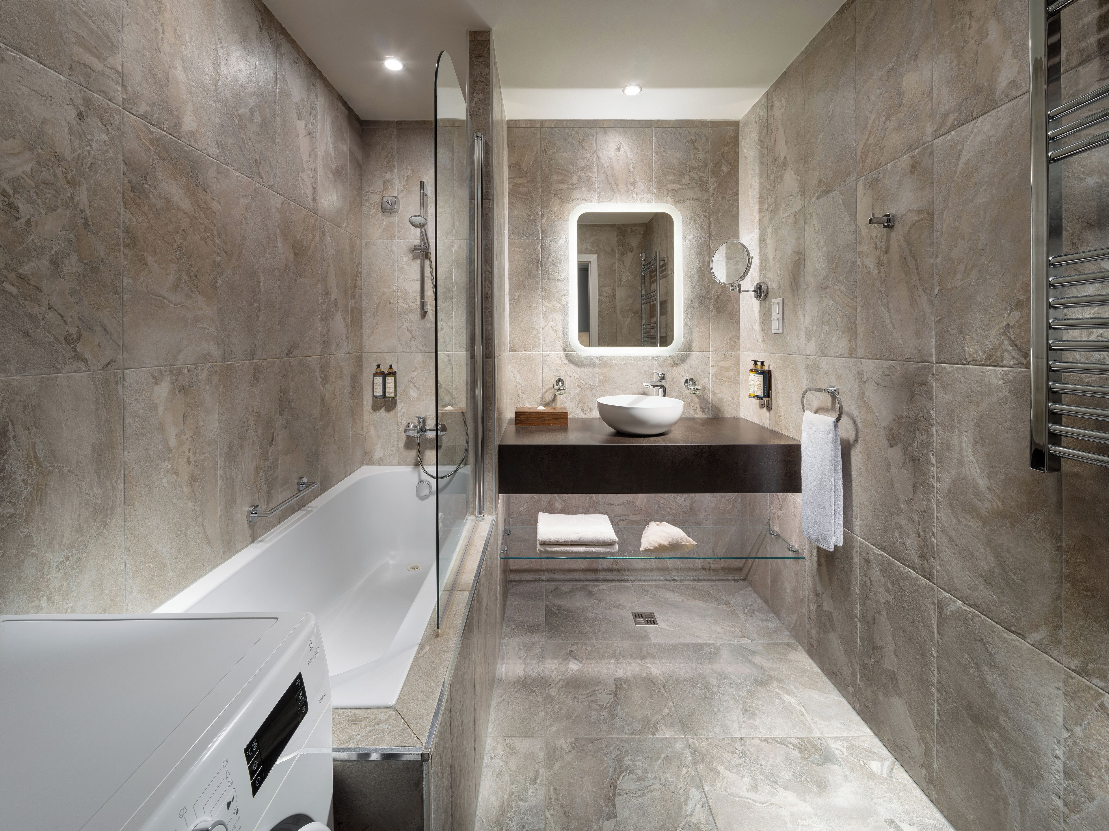 Un baño moderno con bañera, ducha con cerramiento de vidrio, lavamanos con encimera de mármol y un perchero para toallas.