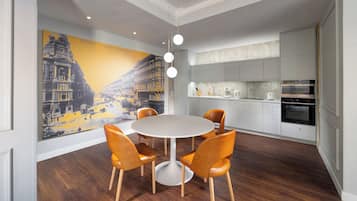 A modern kitchen with white cabinets, a built-in oven, and a dining area with a round table and orange chairs.