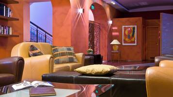 A modern lounge area with leather seating, a glass coffee table, and a bookshelf.