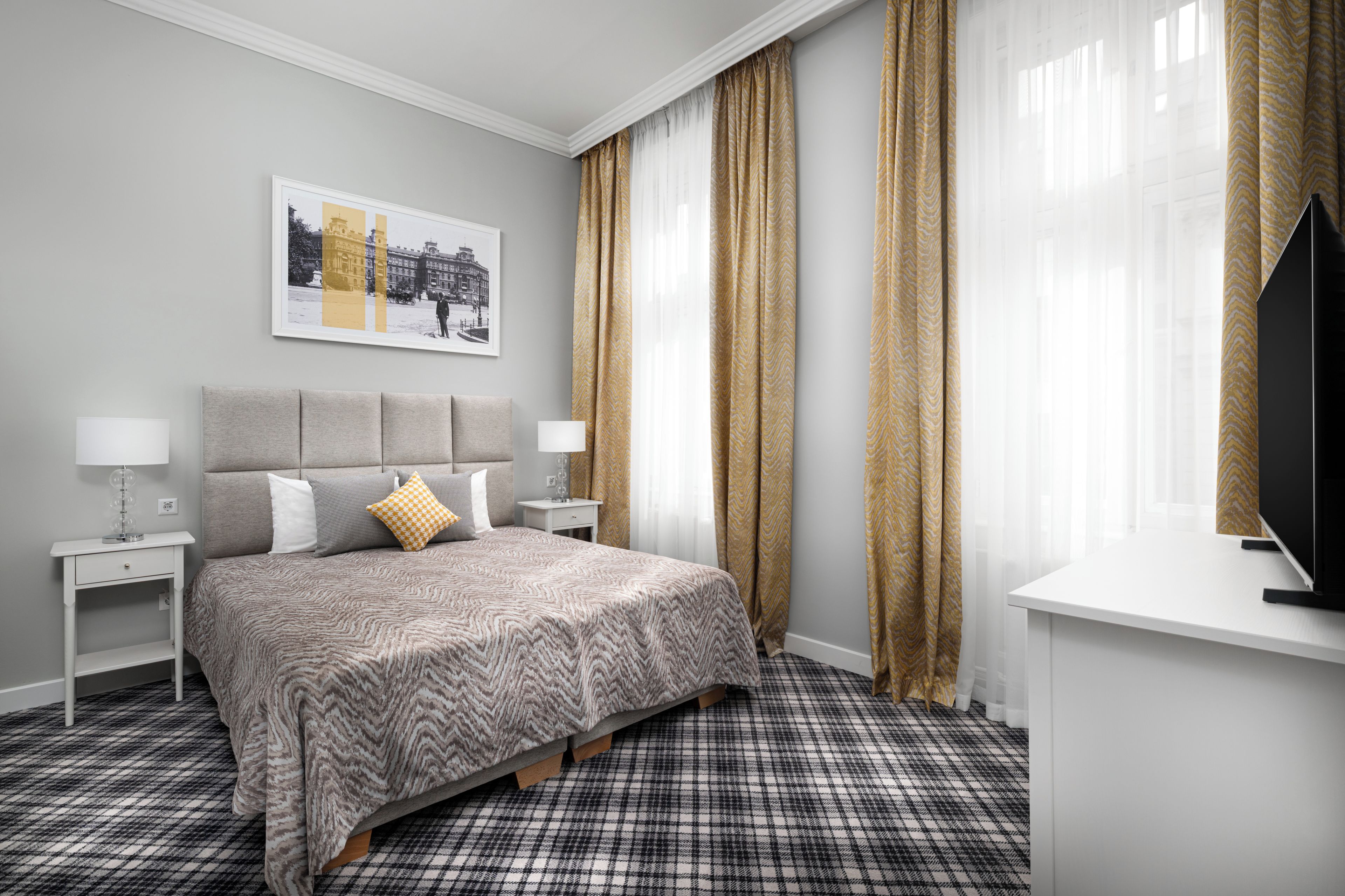 Una habitación de hotel con una cama, una mesita de noche, una lámpara, un televisor y un ventanal con cortinas.