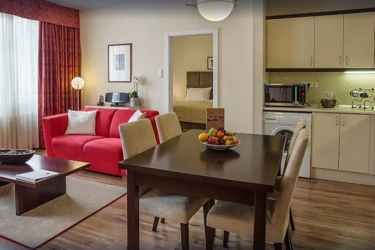 Un espace de vie compact comprenant un canapé rouge, une table à manger avec des chaises, un téléviseur et un coin cuisine équipé d’un four à micro-ondes et d’un grille-pain.