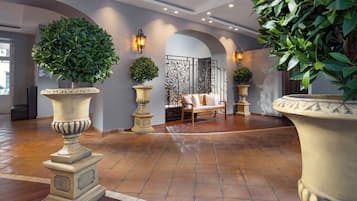 Eine geräumige Lobby mit einer hölzernen Bank, großen Kübelpflanzen und einer Wand mit einer Metallgitterverkleidung.