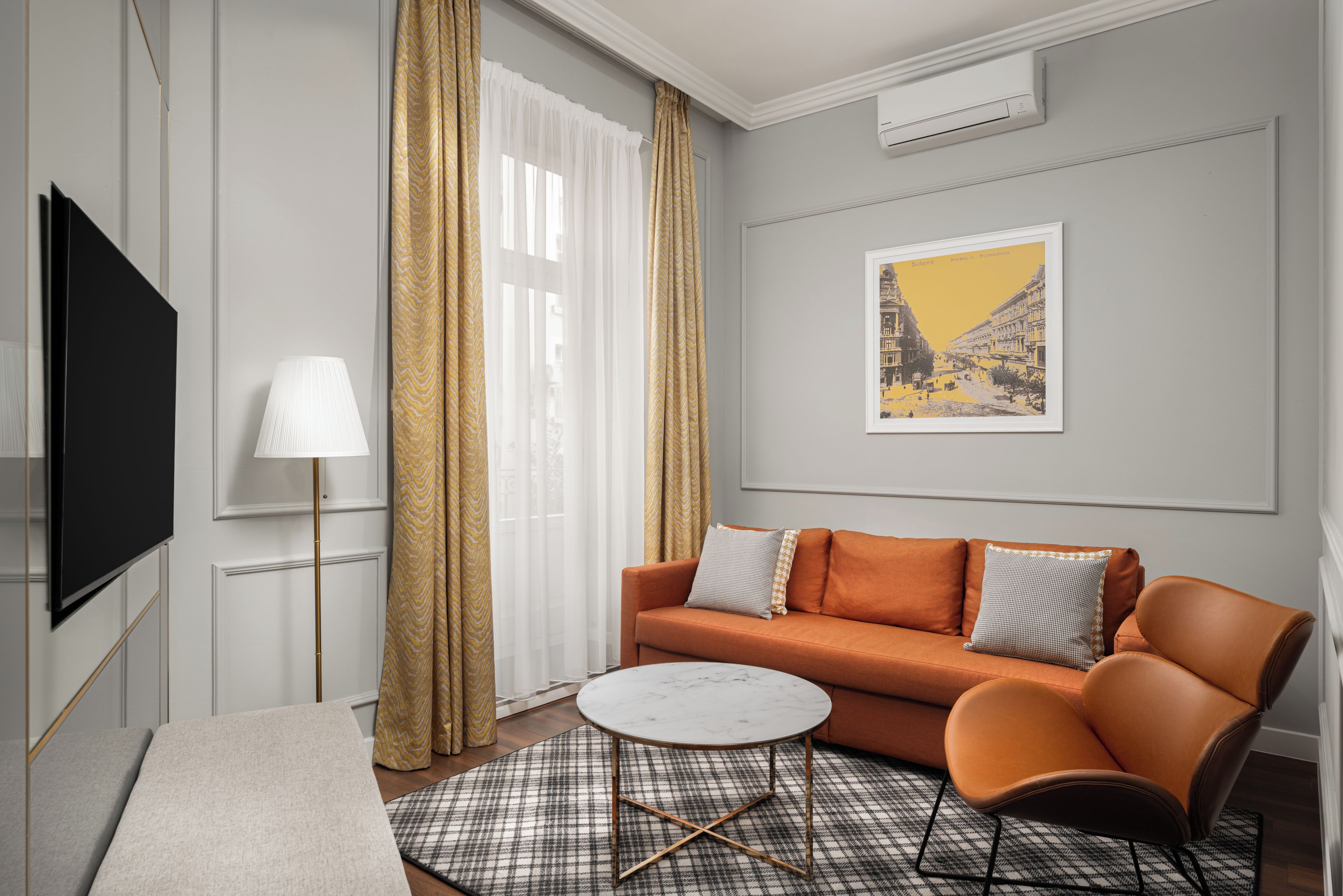 Una habitación de hotel moderna con sofá, sillón y televisor de pantalla plana.