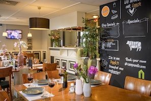 A restaurant with tables set for dining, a chalkboard menu, and a television in the background. - Campanile Hotel Rotterdam - Oost (Rotterdam)