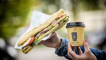 Una persona sosteniendo un sándwich y una taza de café.