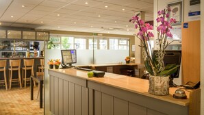 A reception area with a wooden counter, a computer, and a vase with purple flowers. - Campanile Hotel Brussel / Bruxelles - Vilvoorde (Vilvoorde)
