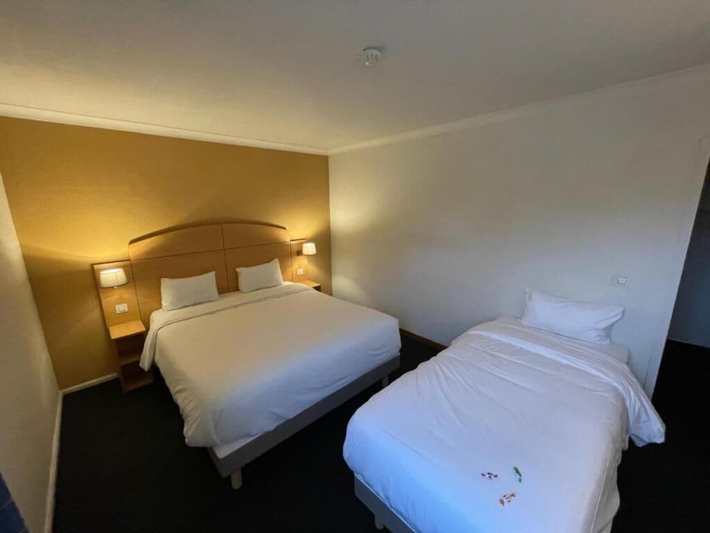A hotel room with two beds, a headboard, bedside lamps, and a carpeted floor.