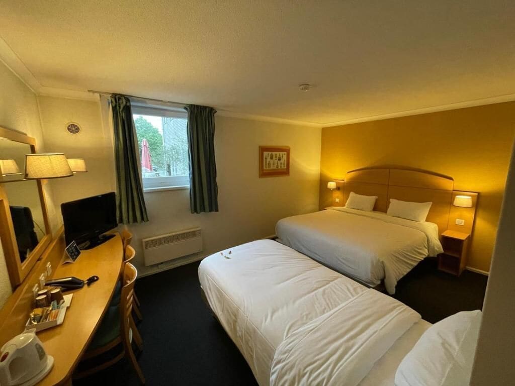Een hotelkamer met een bed, nachtkastje, lamp en een raam met gordijnen.