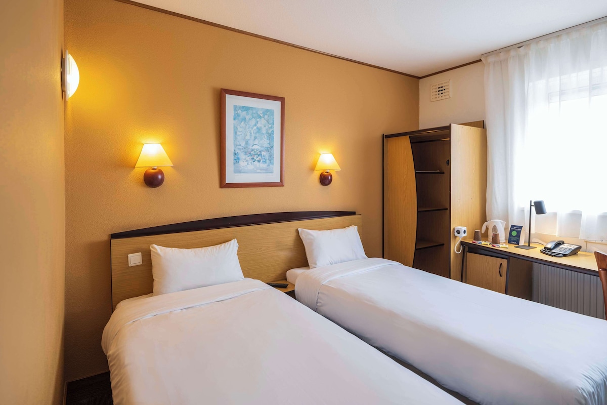 Een hotelkamer met twee bedden, een bureau met telefoon, een lamp en een schilderij aan de muur.