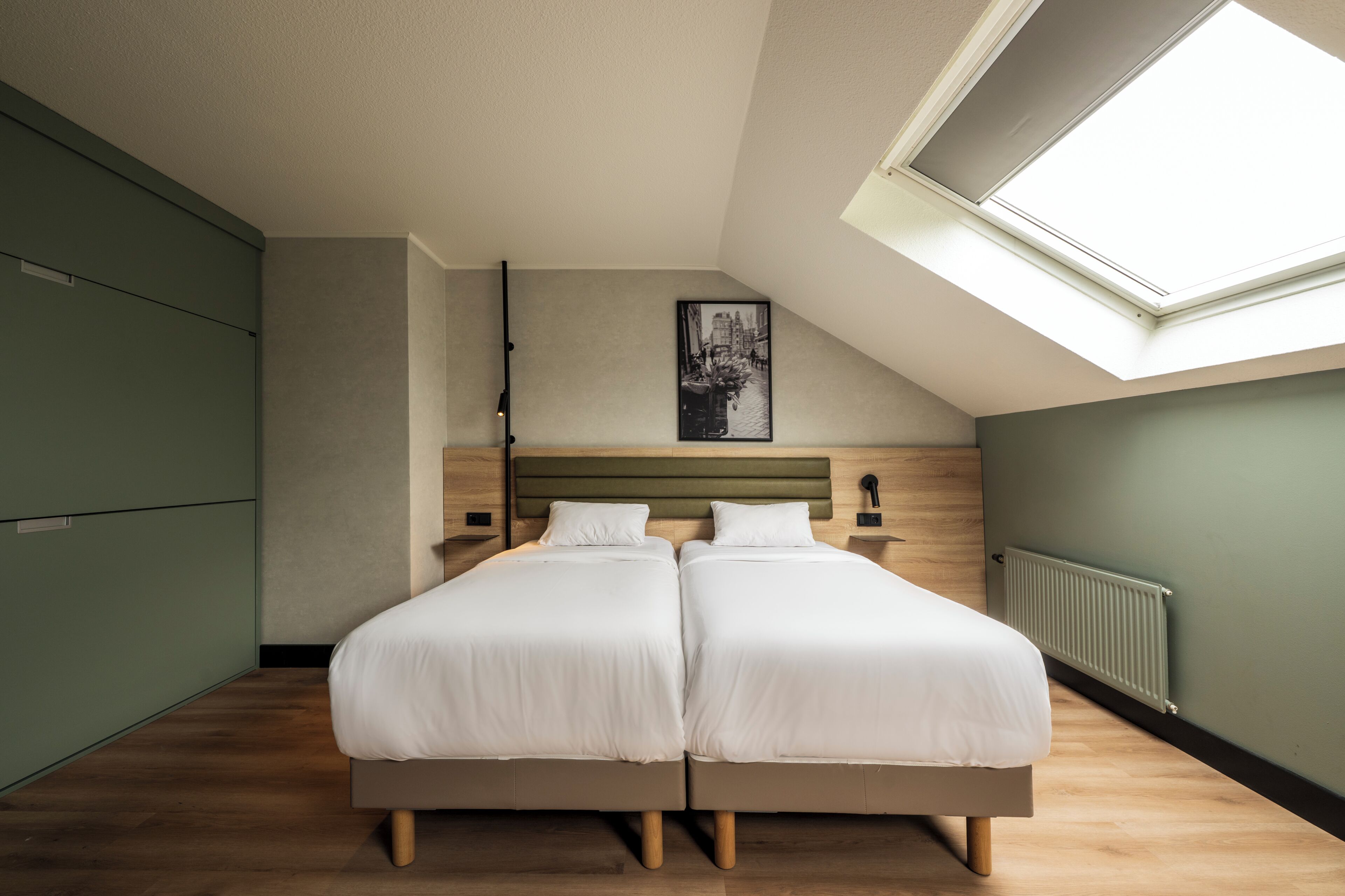 A bedroom with two beds, a skylight, a radiator, and a framed picture on the wall.