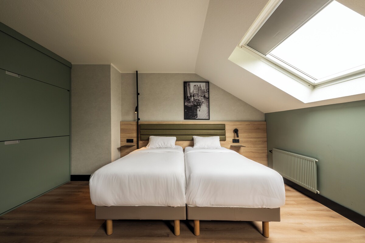 Een slaapkamer met twee bedden, een dakraam, een radiator en een lijst met een afbeelding aan de muur.