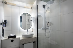 Een moderne badkamer met een ronde spiegel, een wastafel, een handdouche en een douche met glazen wanden.