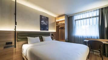 Hotelkamer met een bed, bureau, stoel, kast en raam met gordijnen.