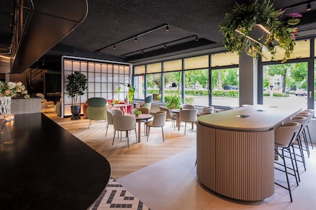 A modern interior with a curved bar, round tables, and chairs, large windows with a view of the street, and indoor plants.. TULIP Hotels & Residences - Zwolle