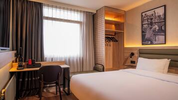 A hotel room with a bed, desk, chair, and a walk-in closet with hanging clothes.