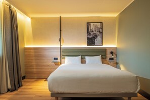 Een netjes opgemaakt bed in een hotelkamer, met een hoofdeinde, een aan de muur bevestigd schilderij en een nachtkastje met een lamp.