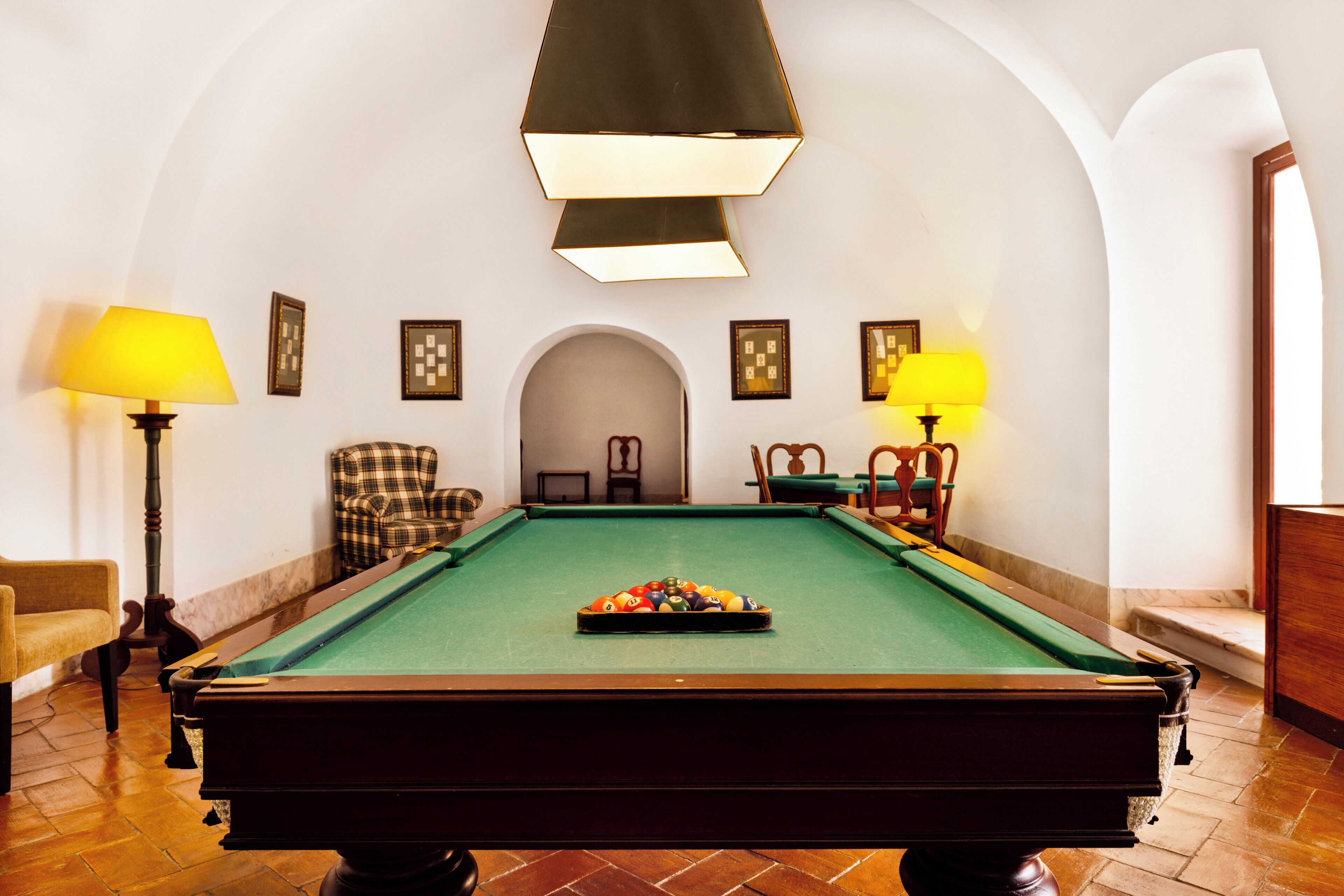 Una sala de billar con mesa de pool, dos lámparas y una silla.
