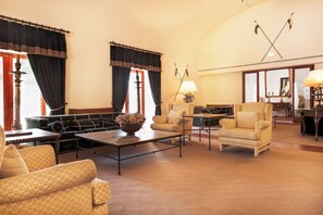 A spacious lobby with a high ceiling, a coffee table, seating arrangements, and a large mirror reflecting the room.