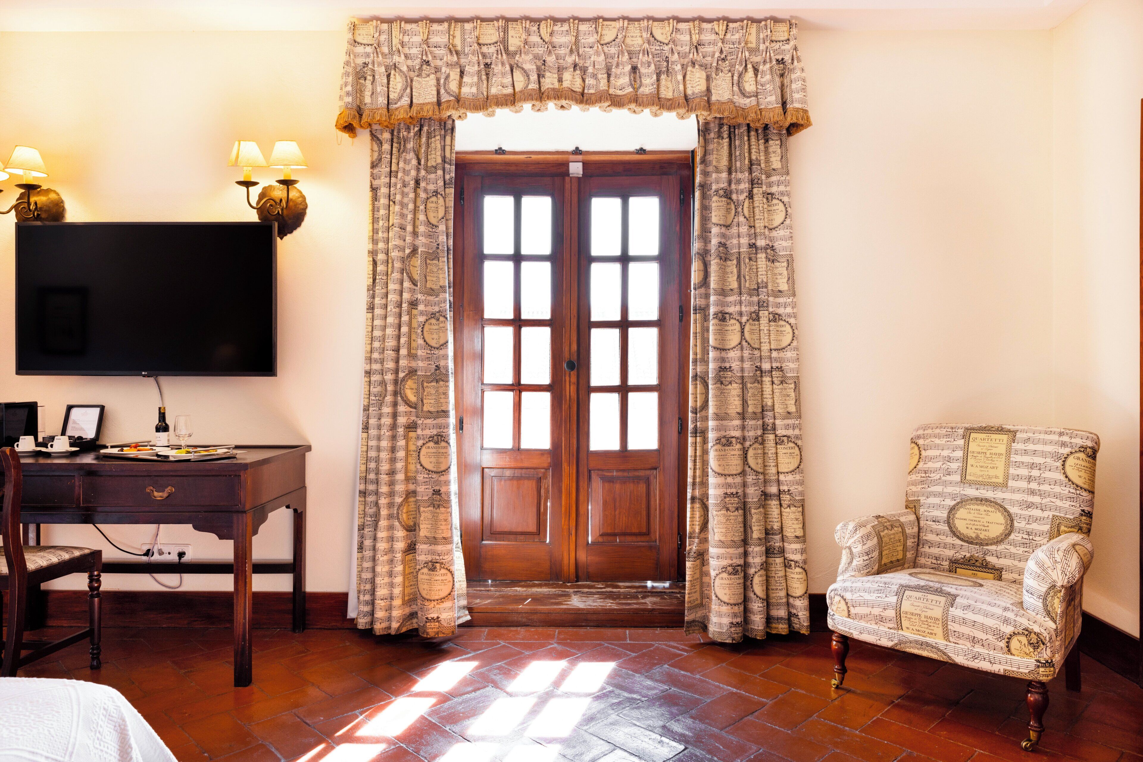 Una habitación con puerta de madera, un escritorio con computadora, una silla y un televisor montado en la pared.