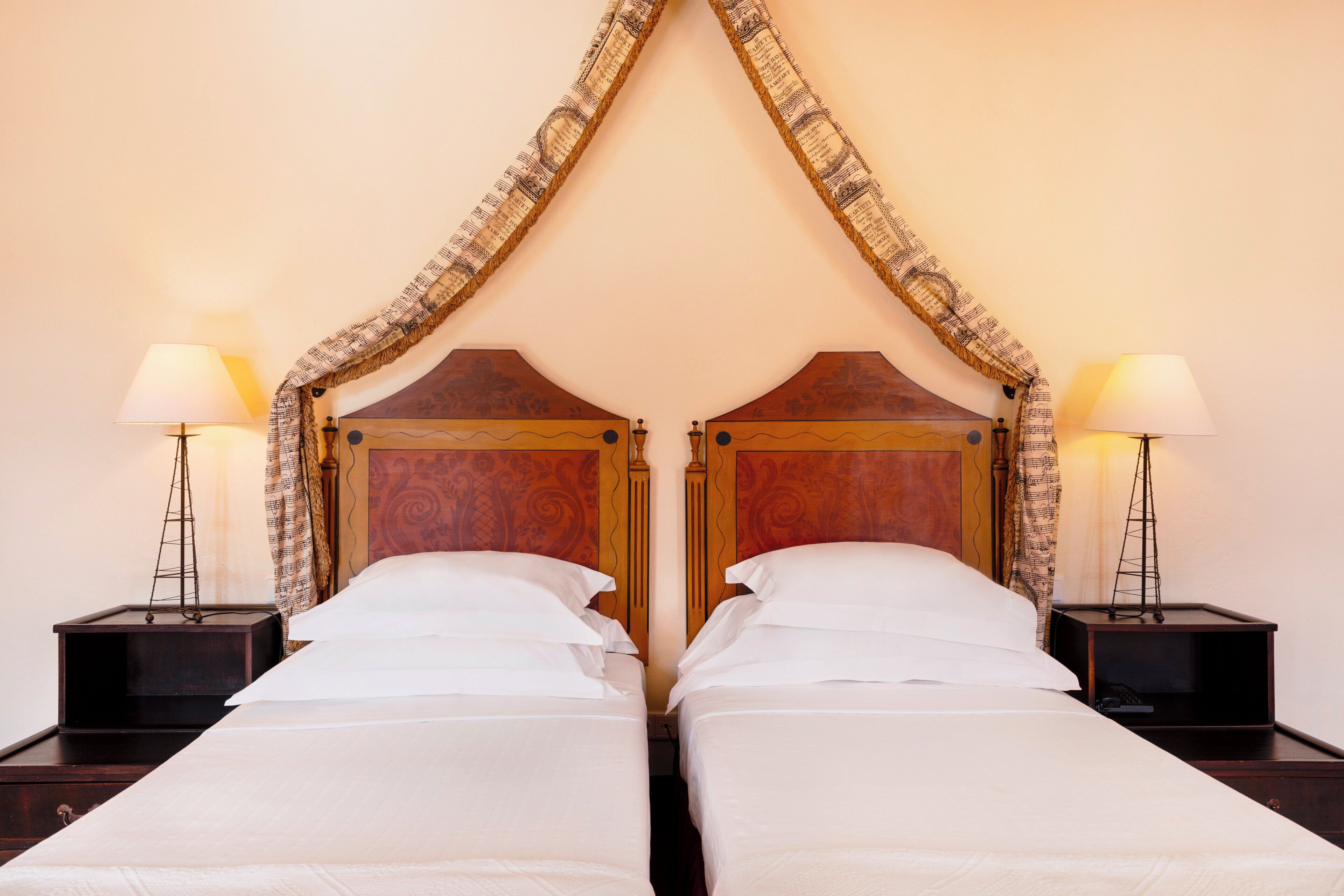 A double bed with a wooden headboard, flanked by two nightstands with lamps, in a room with plain walls.