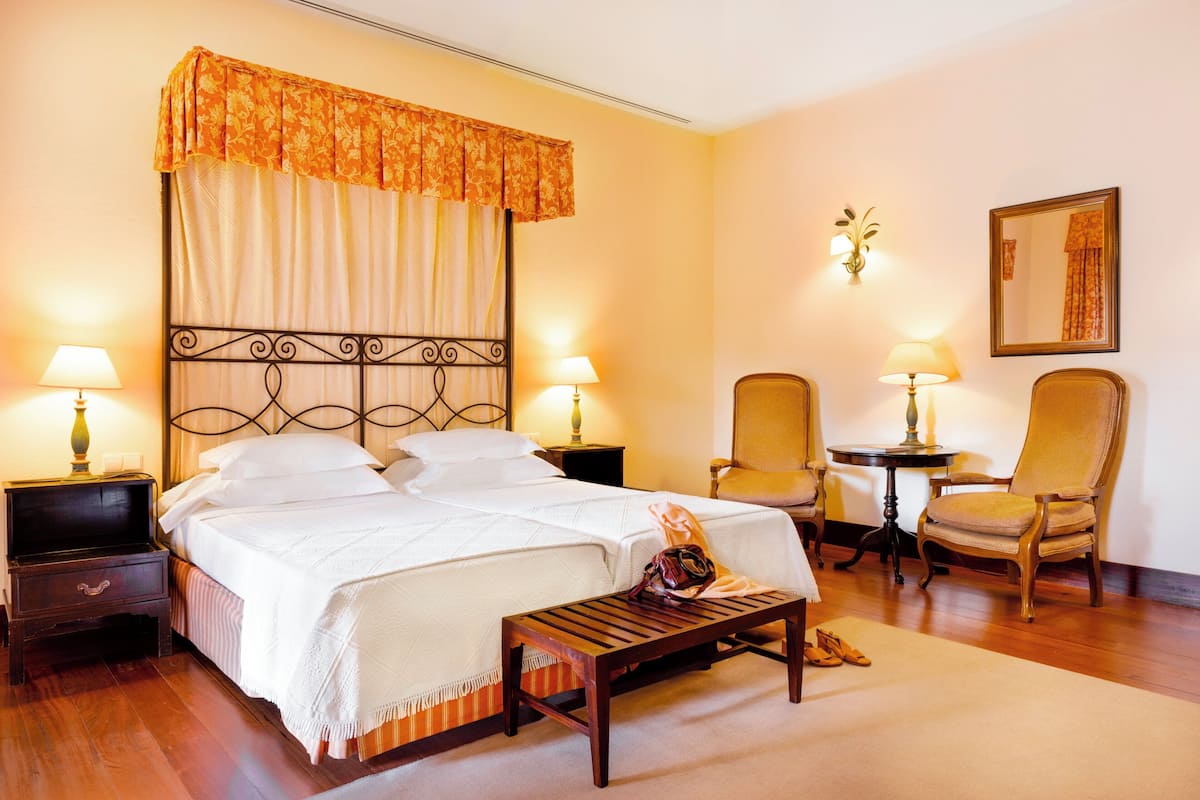 A hotel room with a bed, two chairs, a small table, and a bench.