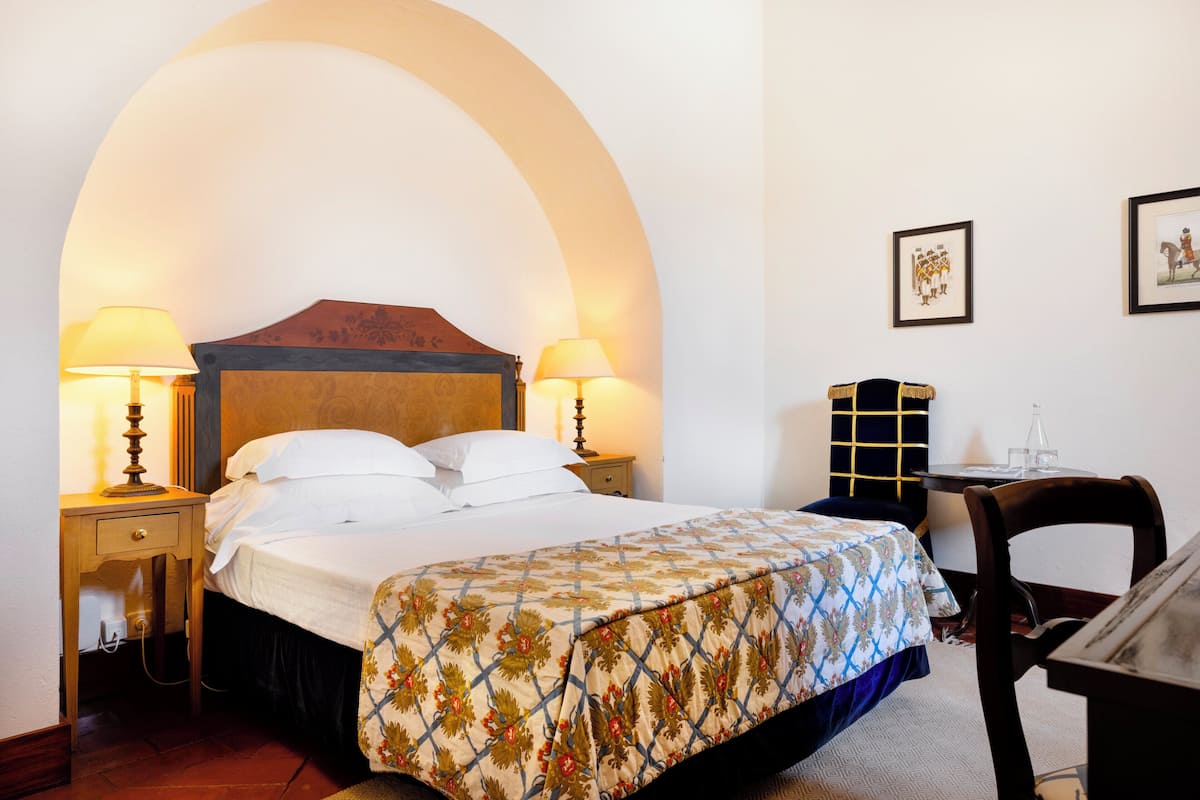 A hotel room with a bed, two bedside lamps, a small table, and a chair.