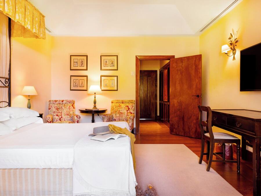 A hotel room with a bed, a desk, a chair, a television, and framed pictures on the wall.