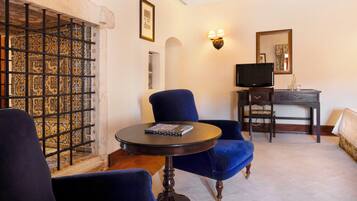 A room with a blue armchair, a small round table with a book, a television on a wooden stand, and a patterned wall.