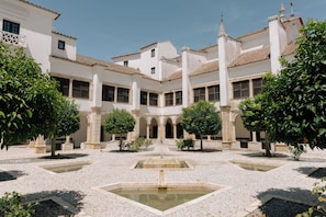 Ein Innenhof mit einem Brunnen, umgeben von weißen Gebäuden mit Bogenportalen und Säulen.