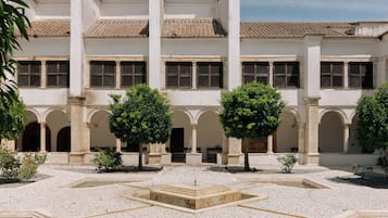 A courtyard with a fountain, surrounded by white buildings with arched doorways and tiled roofs.