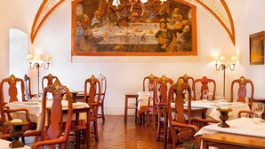 A dining area with ornate wooden chairs, tables set with white tablecloths, and a large painting above the tables depicting a historical scene. - Pousada Convento de Vila Viçosa - Historic Hotel (Vila Vicosa)