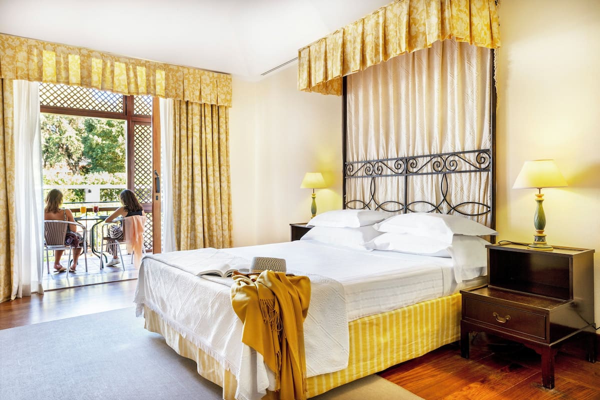 A hotel room with a bed, bedside tables, a window with curtains, and a view of the outside.