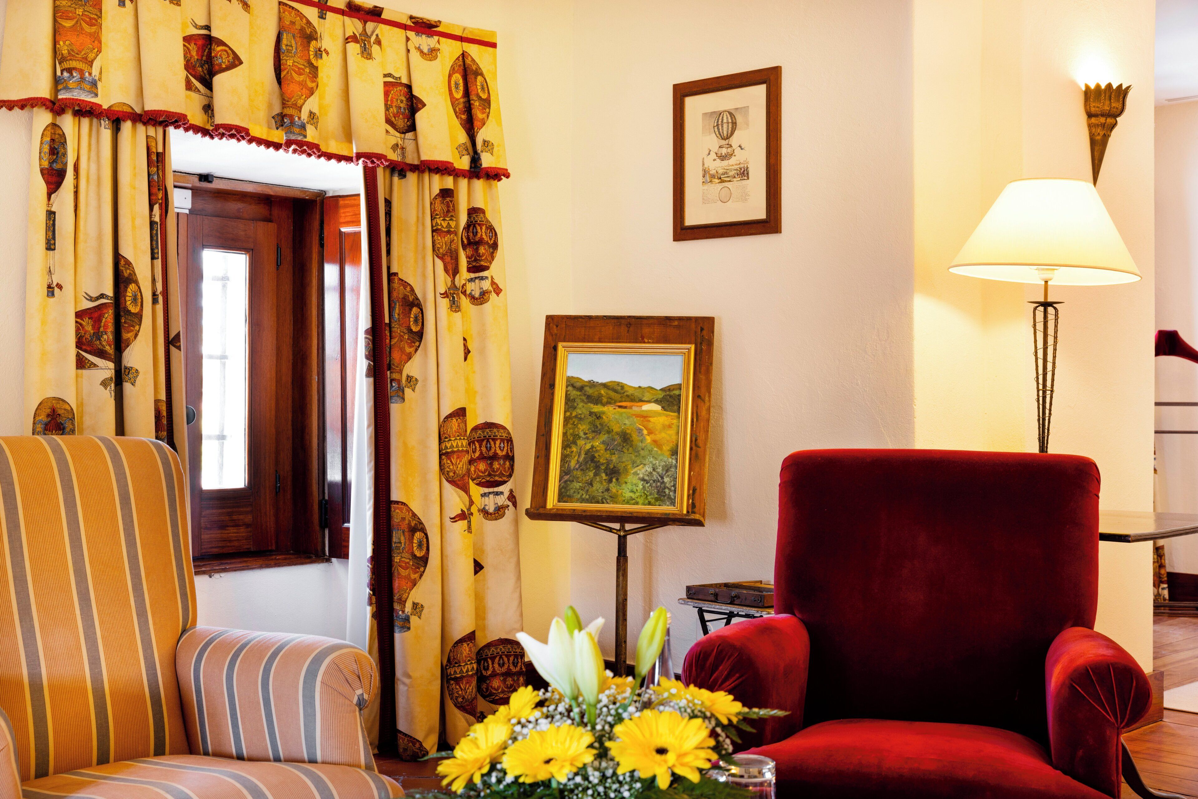 Una habitación con un sofá a rayas, un sillón rojo, un cuadro en la pared y una lámpara.